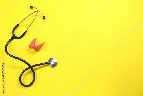 Endocrinology. Stethoscope and model of thyroid gland on yellow background, top view. Space for text