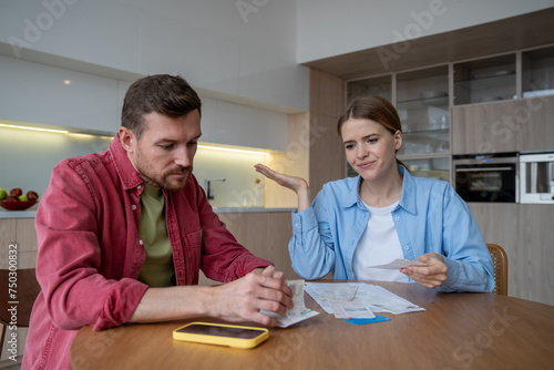 Upset married couple have difficulty paying bills. Husband and wife resentfully rearrange numerous receipts on kitchen table. Preoccupation with financial problems spouses think about budget planning