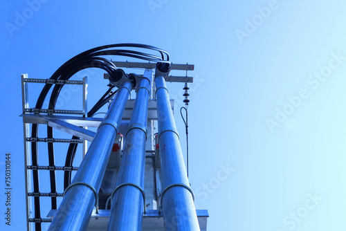 Three metal conduit pipes. High voltage conduit with clamps installed on the side of a concrete pole with transformer system cables on a blue sky background in bottom view with selective focus.