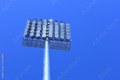 Closeup of stadium lights. Set of spotlight panels for outdoor stadium lighting on tall masts in bottom view on blue sky background with copy space with selective focus.