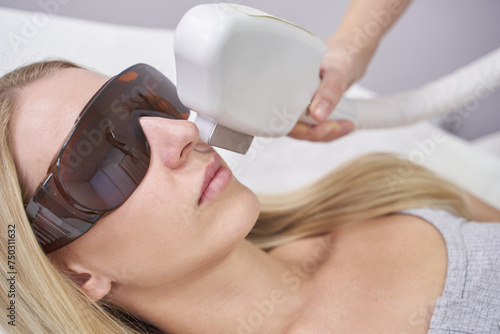 Laser facial treatment for hair removal and rejuvenation at spa. White equipment enhances beauty and skin care. The cosmetologist uses advanced technology for therapy, promoting health, cosmetic care