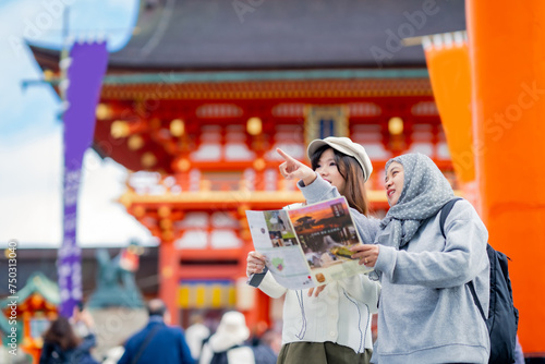 Travel, muslim, Two Asian female tourists of different religions friends visitor learning about history of fushimi inari shrine in travel book while walking through senbon torii path in Kyoto Japan. photo