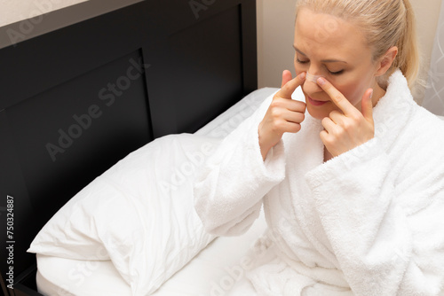 White Woman Applies Nasal Strip on Nose Before Going To Bed, Sitting on Bed. Stop Drug-free, Snoring, Sleeping Apnea Solution. Copy Space. Adhesive Bandage For Better Healthy Breathing. Horizontal. photo