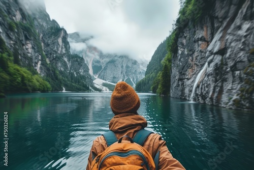 Solo Adventurer in Orange Beanie Contemplating Majestic Mountain Lake Landscape Surrounded by Misty Cliffs