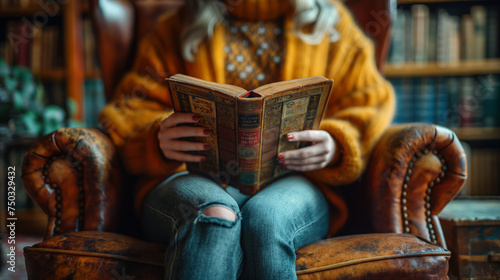 A close-up photo of a person holding a book in their hands, reading and relaxing in a comfortable armchair.