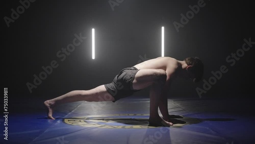 young athletic man doing stretches yoga position, side view in dark studio setting photo