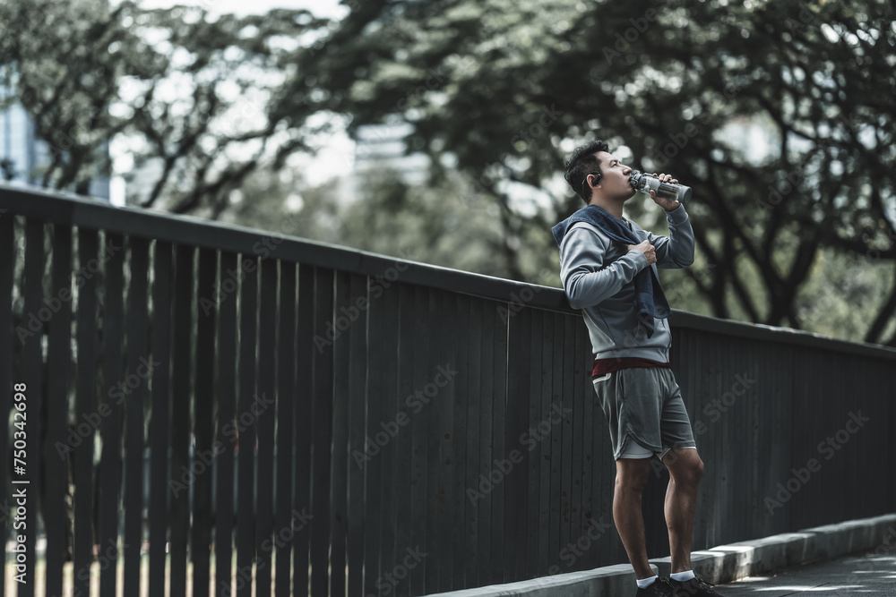 Young sport man drink water after jogging, running in the park. Sport thirsty and resting after exercise. Health and Lifestyle in big city life concept.