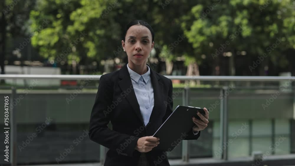 Serious Charming Lady Boss Standing Outside Holding the Documents and Looking at the Camera. Serious Woman with Folder for Paper Outdoor Near the Office Posing. People and Business Concept Serious Charming Lady Boss Standing Outside Holding the Documents and Looking at the Camera. Serious Woman with Folder for Paper Outdoor Near the Office Posing. People and Business Concept