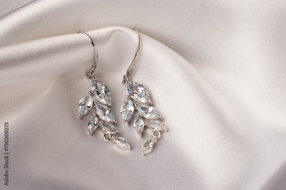 Silver earrings with diamonds on beige silk background Silver earrings with diamonds on beige silk background