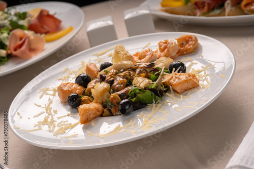 Salad with seafood, grilled salmon and black olives on a white plate