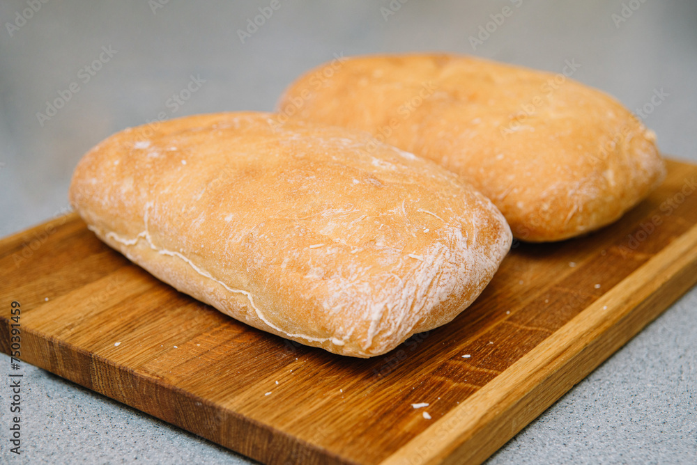 Freshly Baked Ciabatta Bread on Wooden Board. Two loaves of crusty ciabatta bread resting on a wooden cutting board, showcasing the art of traditional baking. Freshly Baked Ciabatta Bread on Wooden Board. Two loaves of crusty ciabatta bread resting on a wooden cutting board, showcasing the art of traditional baking.