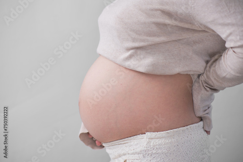 The mature Asian woman stood on the white backdrop, gracefully unveiling her large round belly, cradling it with both of her hands.