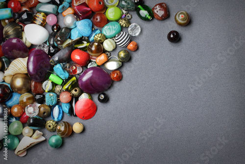 Composition of jewelry making supplies, colorful shiny mixed beads, pliers and craft wire on a gray fabric background, close up. photo