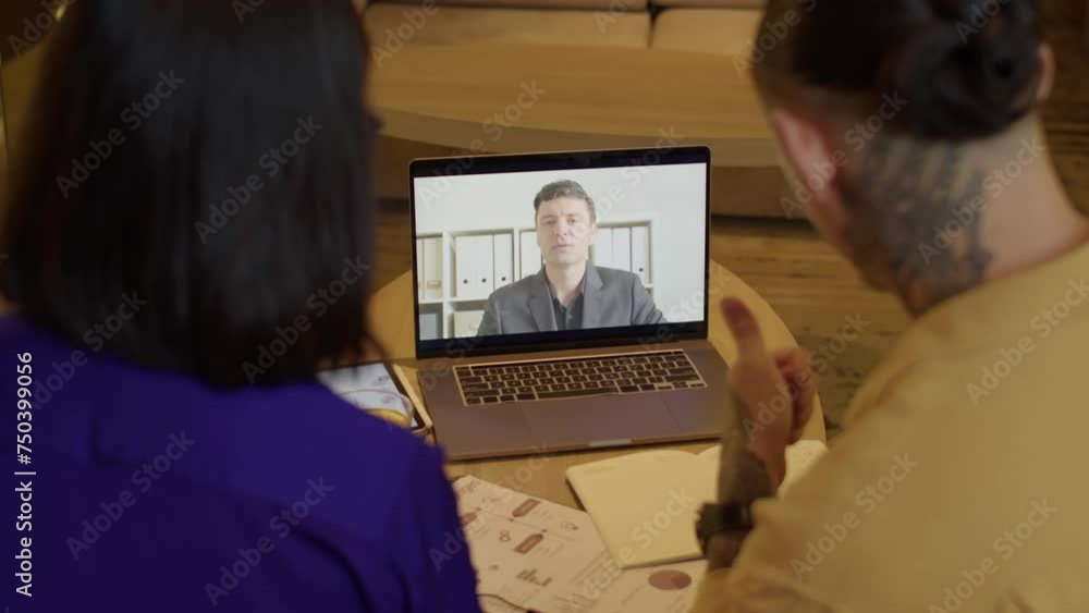 Rear view of coworkers calling to chief manager on video sitting in front of laptop at office Rear view of coworkers calling to chief manager on video sitting in front of laptop at office