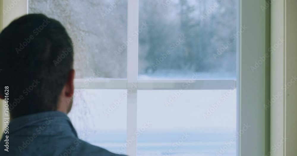 Young man drinking morning coffee and looks through window to snowy landscape. Winter Solitude Young man drinking morning coffee and looks through window to snowy landscape. Winter Solitude