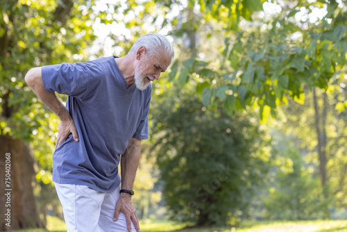 Foto Senior gray-haired man with a beard jogging in the park and doing sports, standing bent over and holding his hand behind his back, felt severe pain and sprain