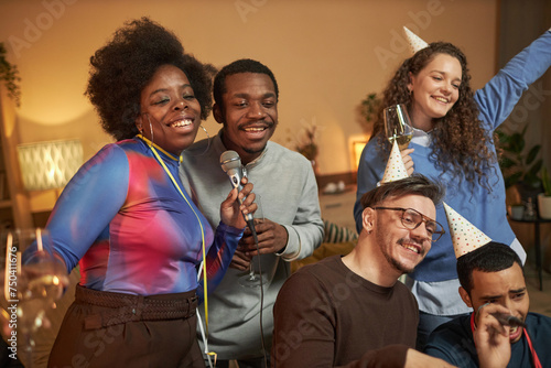 Multiethnic group of adult friends enjoying karaoke at house party and singing to microphone together