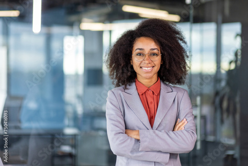 Smiling young African American businesswoman, owner standing in business suit and glasses in office, crossed arms on chest and looking confidently at camera. photo