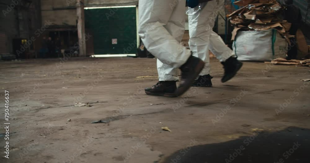 Close-up shot of two men in white uniforms and black shoes walking along the huge hall of a waste processing plant. Two male colleagues walk with their feet on the floor in a large waste recycling Close-up shot of two men in white uniforms and black shoes walking along the huge hall of a waste processing plant. Two male colleagues walk with their feet on the floor in a large waste recycling