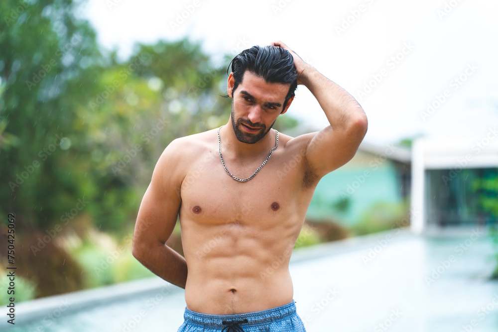 Fototapeta premium Feel the sun and music by the pool. A handsome man is refreshing in the pool water and listening to his favorite song. Swimming and sunbathing, hot summer day and enjoying summer days and rest