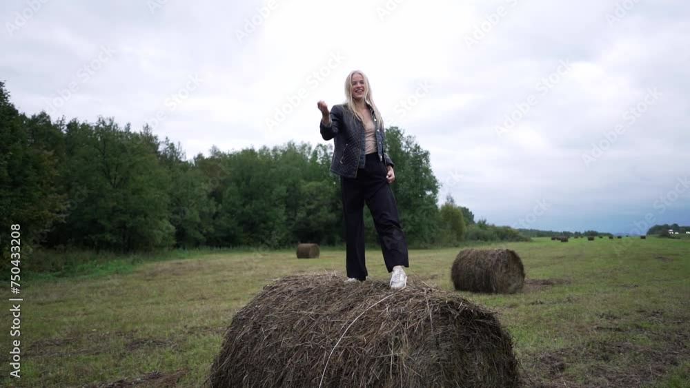 A young woman poses and dances while standing on a haystack. A young woman poses and dances while standing on a haystack.