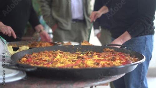 Serving Paella to a gathering of people celebrating. Spanish traditional dish coocked on a pan with meat, pepper and rice. photo