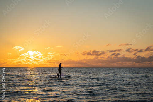 Black sunset silhouette of paddle boarder standing on SUP. Lone paddle board surfer man is surfing on a sup board on calm water at sunset. 