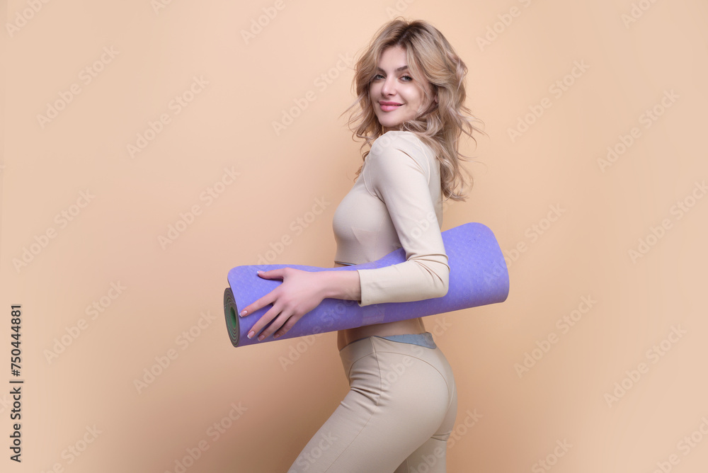 Fit sexy woman holding yoga mat over beige isolated background, copy space. Yoga girl concept. Young strong sporty athletic fitness trainer instructor woman. Workout sport concept. Fit sexy woman holding yoga mat over beige isolated background, copy space. Yoga girl concept. Young strong sporty athletic fitness trainer instructor woman. Workout sport concept.