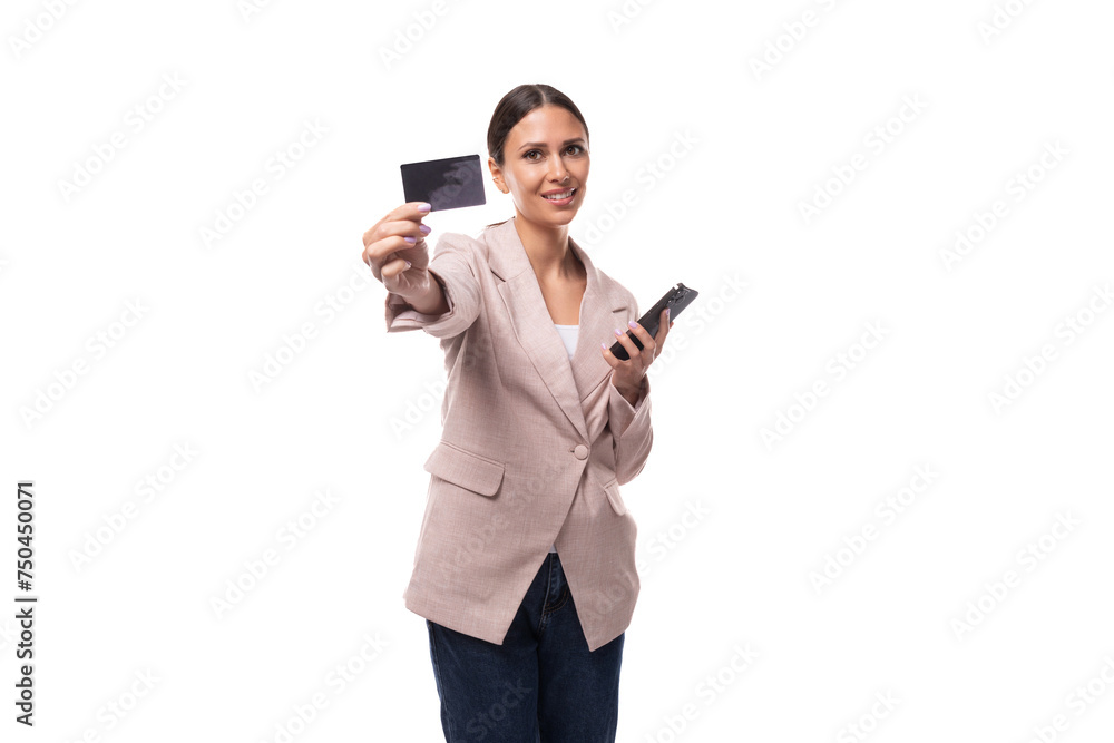 pleasant young woman with black hair in a jacket holding a credit card and a smartphone on a white background with copy space pleasant young woman with black hair in a jacket holding a credit card and a smartphone on a white background with copy space