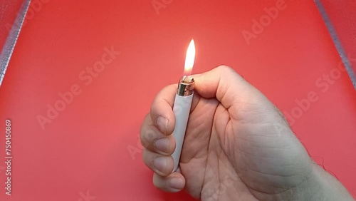 Lighter in man's hand. Close-up hand lights a lighter with sparks on a red background.  photo