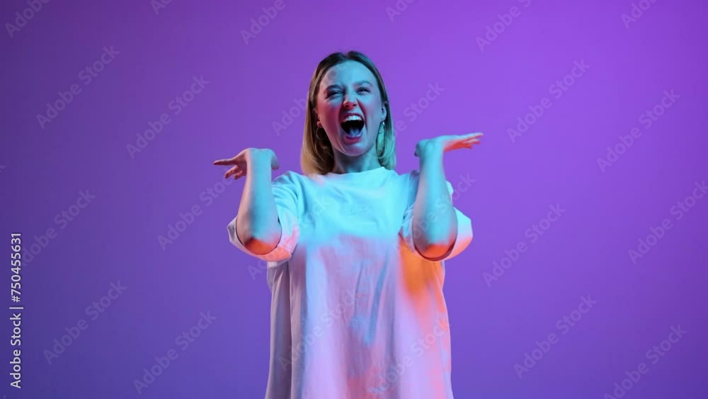 Happy and excited young girl in white t-shirt posing with smile against purple studio background in neon light. Surprise. Concept of youth, human emotions, casual fashion, lifestyle, celebration Happy and excited young girl in white t-shirt posing with smile against purple studio background in neon light. Surprise. Concept of youth, human emotions, casual fashion, lifestyle, celebration