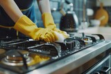 A person in yellow gloves cleaning a gas stove. Ideal for household cleaning or kitchen maintenance concepts