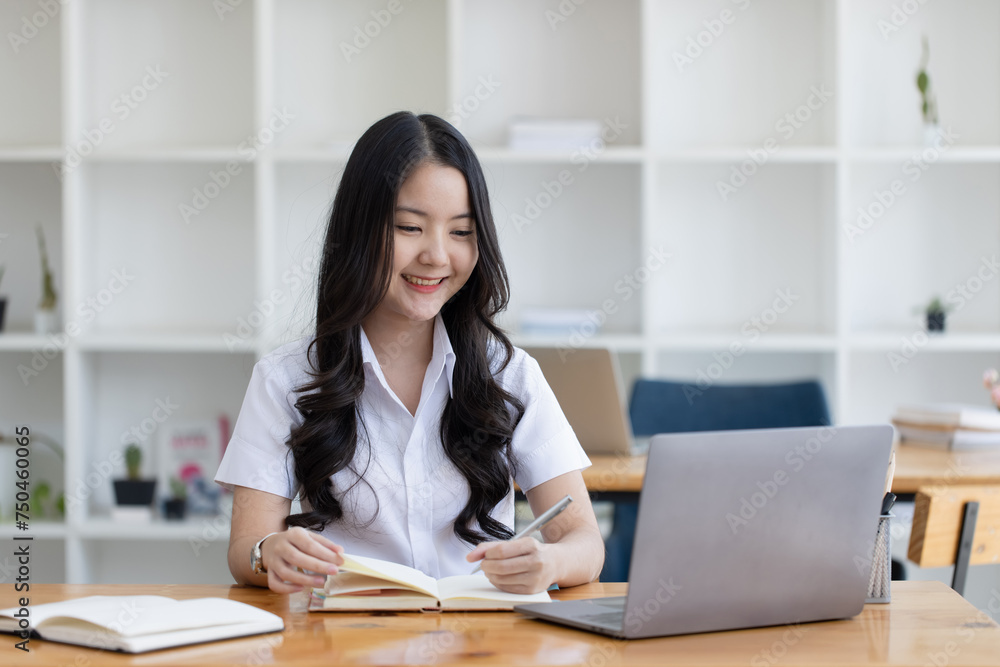 Happy young asian woman wearing earphones and using laptop computer at desk in office, Female asian student with laptop computer, College female student learning online. Happy young asian woman wearing earphones and using laptop computer at desk in office, Female asian student with laptop computer, College female student learning online.
