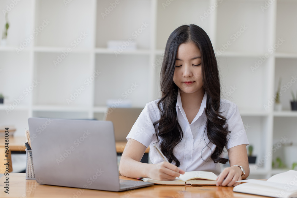 Happy young asian woman wearing earphones and using laptop computer at desk in office, Female asian student with laptop computer, College female student learning online. Happy young asian woman wearing earphones and using laptop computer at desk in office, Female asian student with laptop computer, College female student learning online.