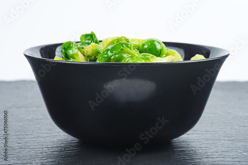 Cooked organic brussels sprouts in black bowl isolated on white background.