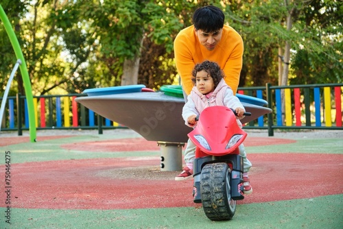 Latin father playing with his one year old daughter on a balance bike in a park.