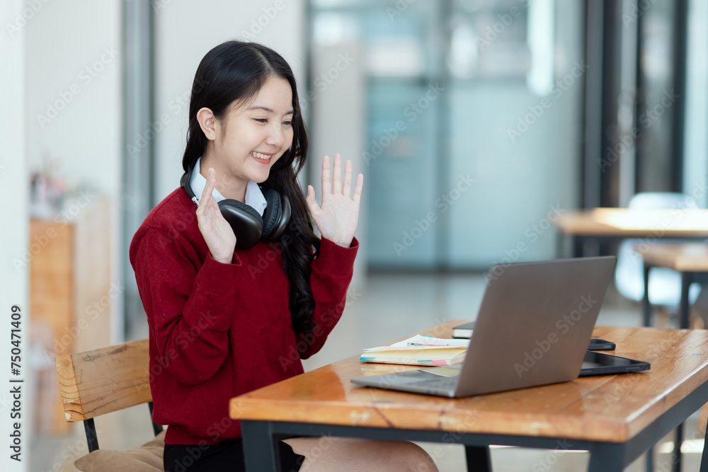 Happy young asian woman wearing earphones and using laptop computer at desk in office, Female student with stack of books and laptop. Happy young asian woman wearing earphones and using laptop computer at desk in office, Female student with stack of books and laptop.