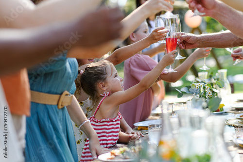 Family clinking glasses at summer garden party, kids clinking with nonalcoholic drink, lemonade. Celebratory toast at table. Big family garden bbq.