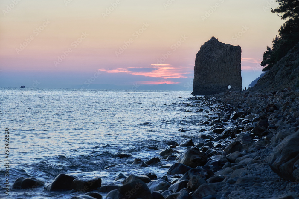 Sun dips below horizon, rocky coastline, nature beauty in serene tranquility. Waves gently lap against shore, while silhouetted cliffs stand majestically against dusky sky