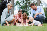 Family playing in grass with wooden garden game. Father, mother, and three children having fun at birthday party.