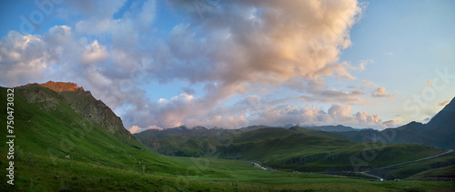 Panoramic view of a lush valley at dusk with the last sunlight touching mountain peaks under a vast cloudy sky