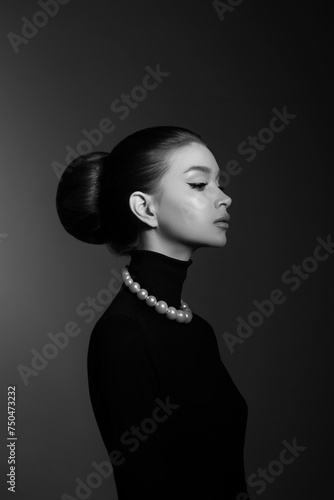 Woman poses confidently, dressed in a stylish black turtleneck and exquisite luxury jewelry. Hair pulled back in a bun, natural cosmetics and make-up
