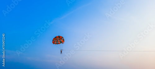 Parasailing extreme sports on beach in blue sky background. Man is parasailing in the blue sky. Paragliding in the clear sky above the sea.