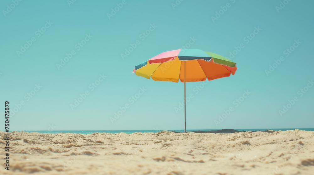 A vivid beach umbrella stands alone on the sandy shore under a clear blue sky, Summertime background.