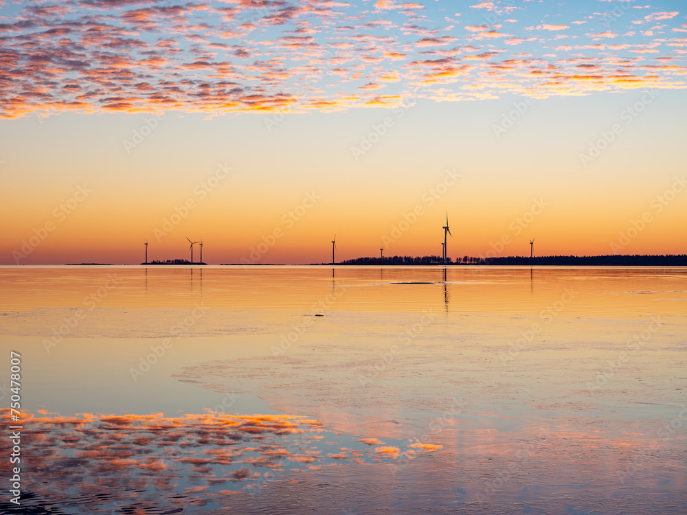 Naklejka premium Colorful sunset by the calm sea with fluffy clouds in the sky and windmills on the horizon, Bothnian Bay, Baltic Sea, Finland