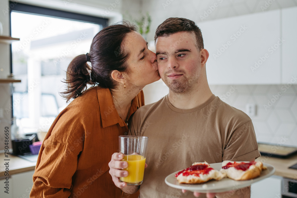 Young man with Down syndrome serving breakfast to his mother as a Mother's Day gift. Concept of Mother's Day and maternal love to disabled children. Young man with Down syndrome serving breakfast to his mother as a Mother's Day gift. Concept of Mother's Day and maternal love to disabled children.