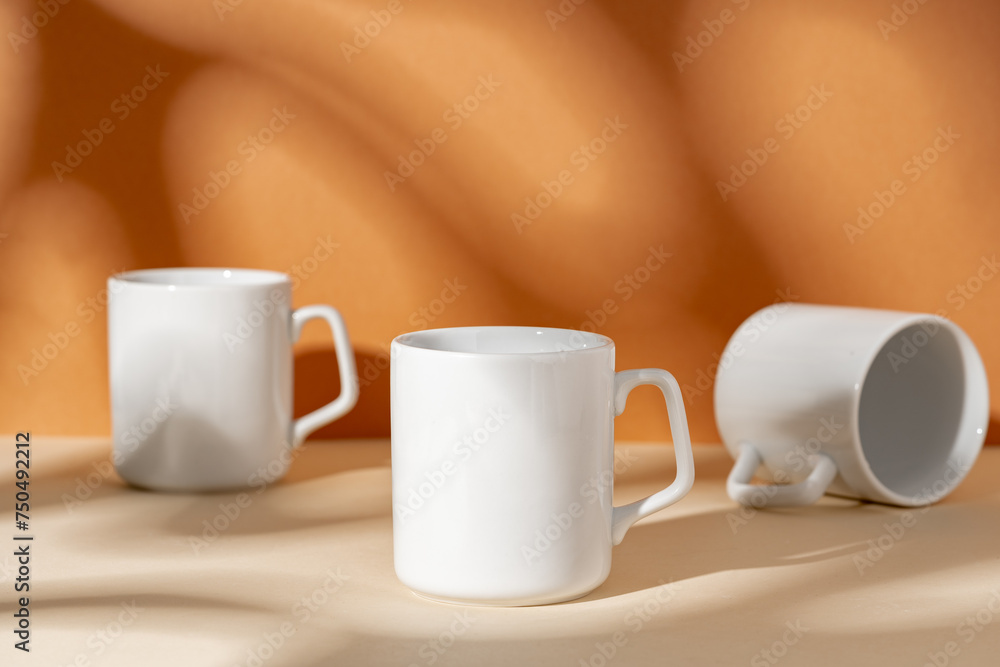 White ceramic mugs on peach background with shadows White ceramic mugs on peach background with shadows