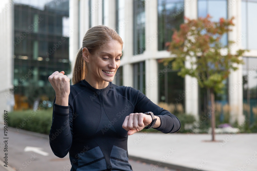 A fit woman with a smile checks her fitness tracker outdoor, exuding happiness and a healthy lifestyle. With a backdrop of urban architecture, this image captures the essence of active living in the A fit woman with a smile checks her fitness tracker outdoor, exuding happiness and a healthy lifestyle. With a backdrop of urban architecture, this image captures the essence of active living in the