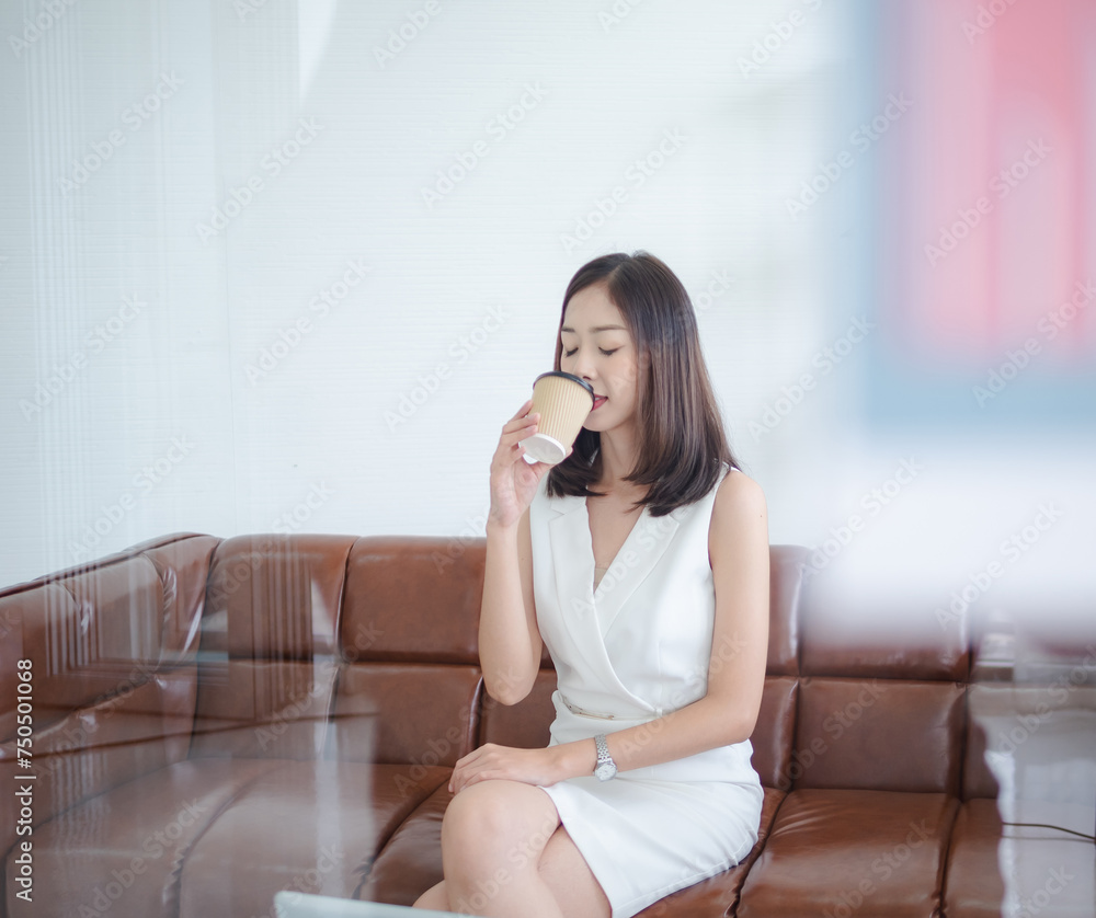 Business girl woman portrait beautiful asian one person sitting on sofa hand holding paper cup hot coffee drimking and looking relax comfortable aroma happy time rest from work inside room office Business girl woman portrait beautiful asian one person sitting on sofa hand holding paper cup hot coffee drimking and looking relax comfortable aroma happy time rest from work inside room office