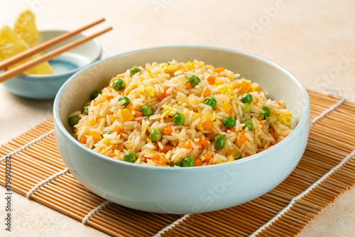 Fried rice with egg and vegetables, onion, bell pepper, carrot, green peas. Prepared and served in a light blue plate, chopsticks.